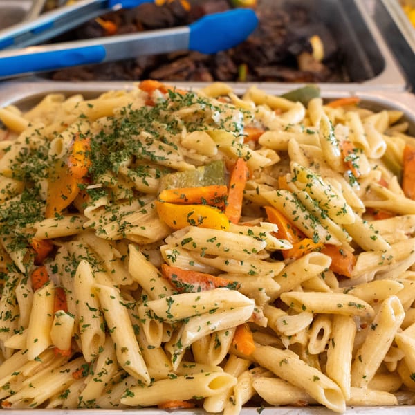 Creamy penne pasta with carrots, bell peppers, and parsley in a serving tray at Peppas Jerk Chicken.
