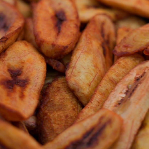 Close-up of golden-brown fried plantain slices, some with darker caramelized spots.