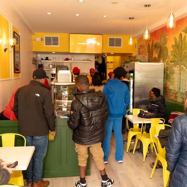 Customers line up at the counter and sit at yellow tables in Peppas Jerk Chicken restaurant.