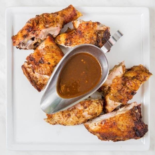 Peppas Jerk Chicken pieces with crispy skin and a metal gravy boat of sauce on a white plate.