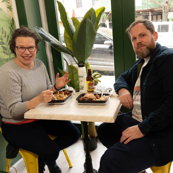 Two customers enjoying jerk chicken meals at a table by a window at Peppas Jerk Chicken.